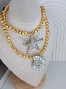 Detail der goldene Perlenkette mit silbernen Seestern- und Spiralmuschel-Anhängern im Lagenlook