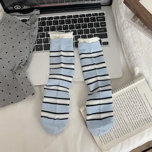 Detail of blue and white striped mid-calf socks with ruffled cuffs on a cozy bed