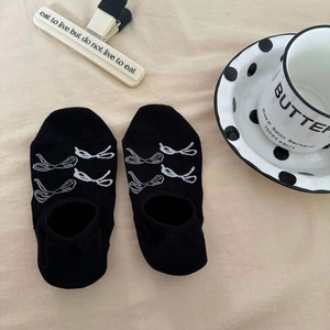 Detailed flat lay of black low-cut socks featuring white bow patterns on beige background