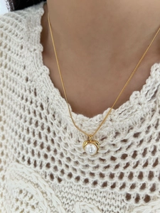 Dettaglio della collana con ciondolo a cuore dorato e perla bianca su modella