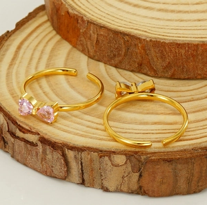 Détail de bagues ajustables en nœud avec zircons cœur roses et clairs sur bois