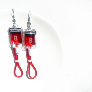 Close-up of blood bag earrings with red filling and Type B blood group label