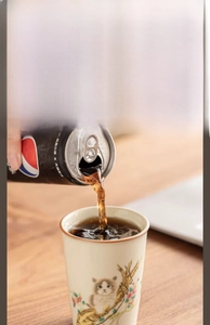 Action shot of Ru kiln cat tea cup being filled with cola on a warm wooden table