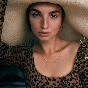 Close-up of minimalist 18K gold stainless steel chain necklace worn with a straw hat