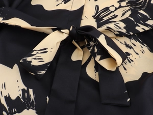 Detailed close-up of the elegant waist tie bow with beige floral print on smooth black fabric