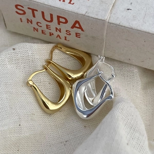Detailed macro view of polished gold and silver U-shaped earrings on textured linen