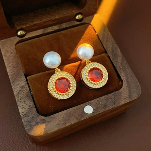 Détail macro de boucles d'oreilles perles plaquées or avec pierre rouge et boîte bois