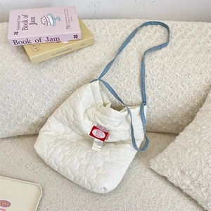 Detail of white heart-quilted shoulder bag with blue strap on soft plush background