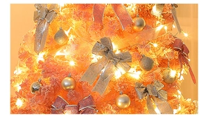 Close-up of pink Christmas tree with silver glitter bows, baubles and warm LED lights