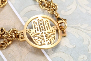 Macro shot of gold double-layer chain bracelet featuring a hollow Hamsa hand pendant