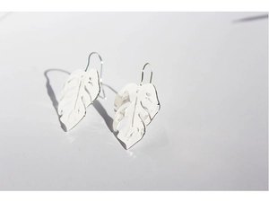 Macro shot of silver hollow monstera leaf earrings with artistic light and shadows