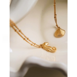 Detailed view of seahorse and shell pendants on a gold bead chain over a ceramic plate