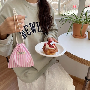 Detailed close-up of a pink striped drawstring pouch held by a hand in a cafe setting