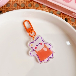 Detail of cute acrylic bear keychain with orange dress and matching metal lobster clasp