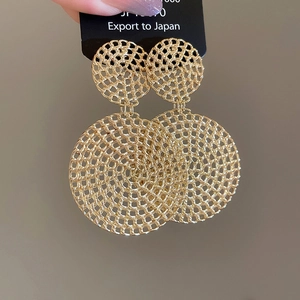 Detail view of gold hollow mesh earrings with intricate woven texture and circular design