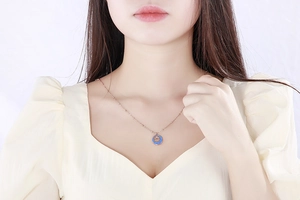 Detail of rose gold clover coin pendant necklace with blue enamel on a model