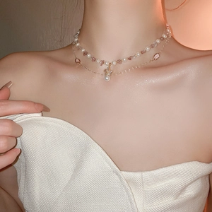 Close-up of double-layer necklace with white pearls and golden crown pendant with gems