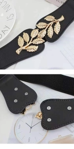 Detail of black elastic belt featuring golden leaf buckle and metallic hook closure