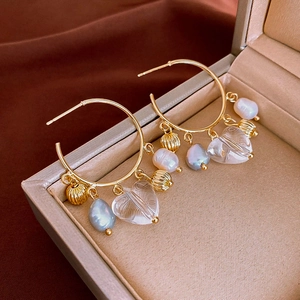 Detail of bohemian gold hoop earrings with baroque pearl and clear heart charms