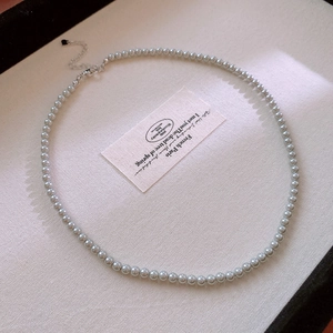 Close-up of elegant grey pearl necklace with silver heart charm on beige fabric
