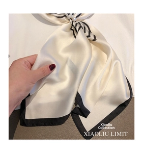 Detail of silky cream square scarf with black contrast borders and a pearl accessory accent