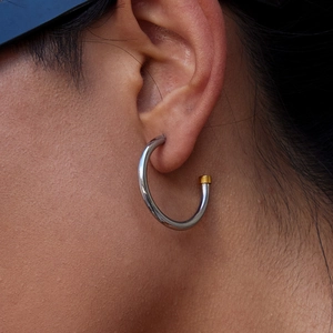 Detailaufnahme der minimalistischen C-förmigen Ohrringe in Silber und Gold auf dem Ohr