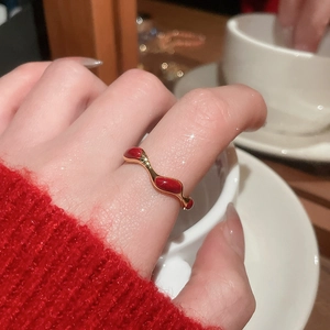 Detail of wave-shaped gold-plated ring with red enamel finish on a model's finger