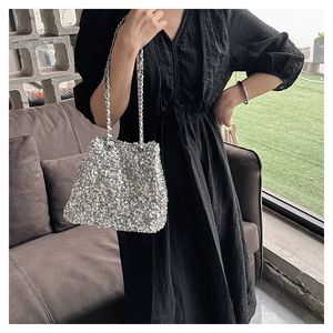 Close-up of silver sequin bucket bag with chain strap styled on a black dress