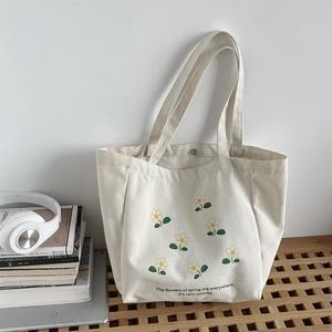 Detailed view of cream canvas tote bag with yellow flowers on a wooden workspace