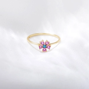 Detail of a gold flower ring with pink gemstones and a turquoise center on silk