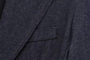 Detail of dark blue denim jacket showing orange contrast stitching and fabric texture
