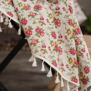 Close-up of linen tablecloth featuring red rose patterns and white fringe tassels