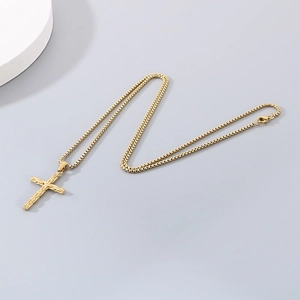 Close-up of golden stainless steel cross pendant with detailed box chain on grey background