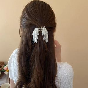 Detailed view of pearl tassel hair claw clip worn on long brown hair in a home setting
