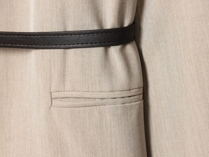 Detail of oat-colored blazer fabric with black slim belt and horizontal pocket seam