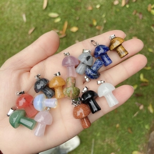Hand holding various 2cm natural crystal mushroom pendants over a natural grass background