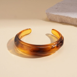 Macro view of amber acrylic open cuff bracelet on a stone textured surface
