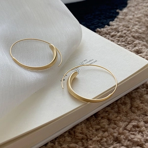 Detail of matte gold hoop earrings with thick curved sections on white silk and books
