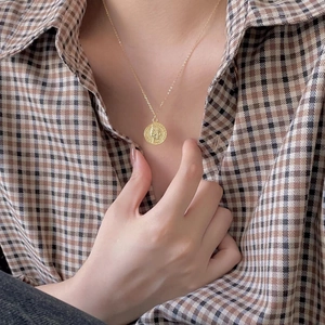 Detail of a vintage gold coin pendant necklace worn over a brown checkered shirt