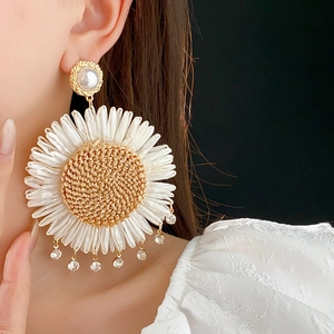 Detailed close-up of large daisy earrings with woven brown center and white petals