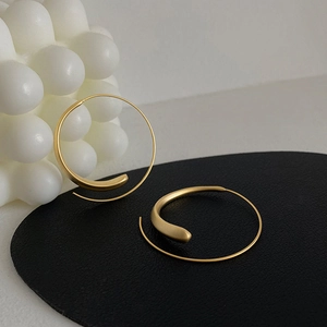 Detailed view of gold hoop earrings with streamlined texture on black leather display