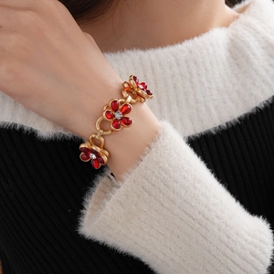 Detailed view of the gold flower bracelet with red gems worn on a wrist over a sweater