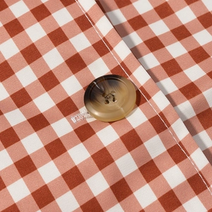 Nahaufnahme von braunem Gingham-Stoff und einem Knopf an einem langen Damenmantel