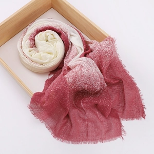 Detail view of a cotton linen scarf with red and white gradient and fringe on a wooden tray