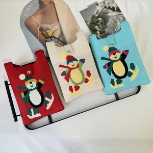 Detailed view of knitted snowman crossbody bags in red, beige and blue on a shelf