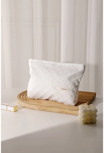 Dettaglio del beauty case bianco trapuntato con logo H&R BAG su vassoio di legno