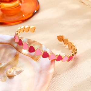 Detalle de brazalete dorado con corazones de esmalte rojo y rosa sobre una concha perlada