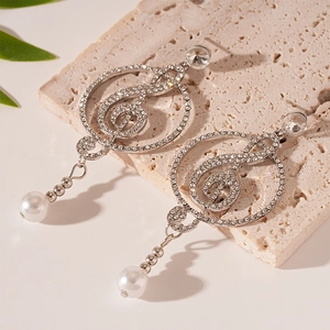 Detail view of treble clef earrings with sparkling rhinestones and white pearls on stone