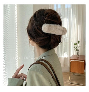 Close-up of beige plush hair claw clip used for styling a bun on brown hair