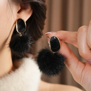 Macro shot of stylish black fuzzy ball drop earrings with gold rimmed oval studs